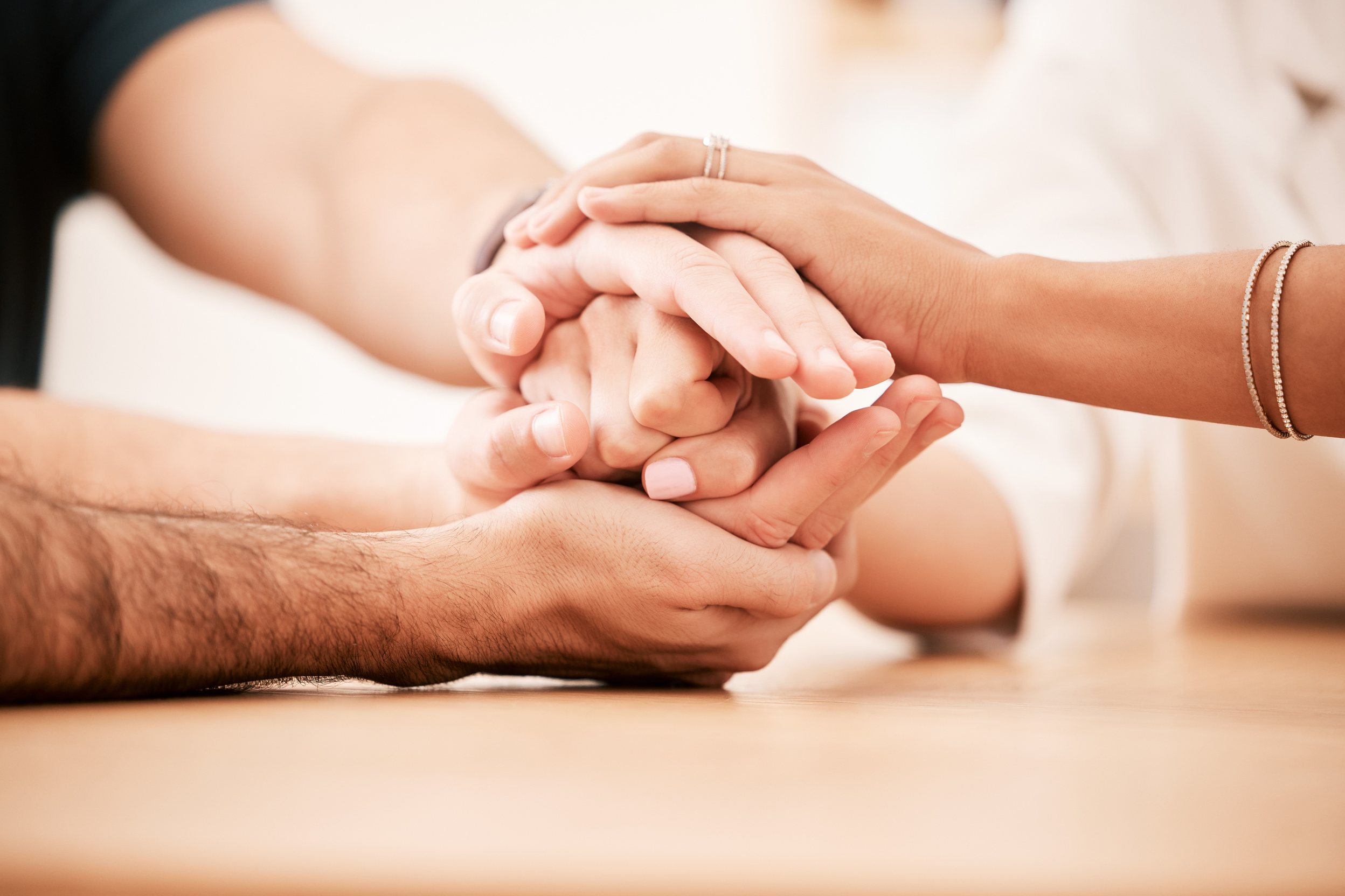 Two people's hands clasped on a table, one pair cupped around the other